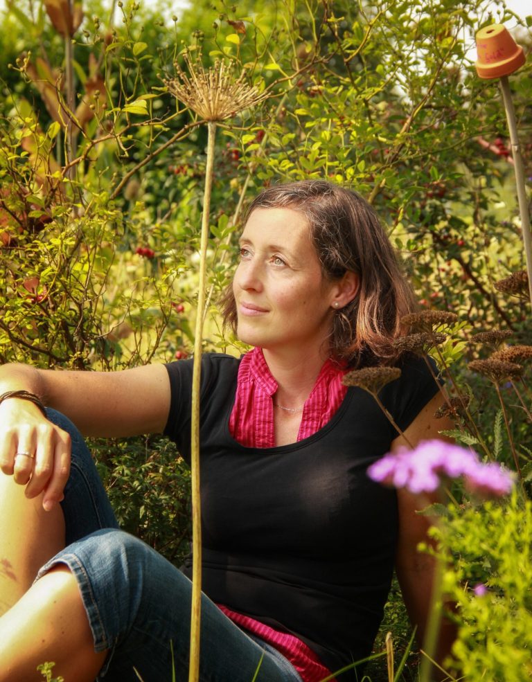 Businessporträt einer Gartengestalterin – aufgenommen in ihrem Garten, umgeben von Pflanzen und natürlicher Atmosphäre.