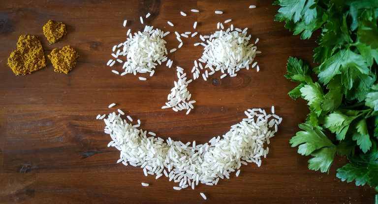 Food-Art mit Bio-Zutaten – Ein Smiley aus Reis auf Holzplatte, verziert mit Gewürzherzen und frischer Petersilie.