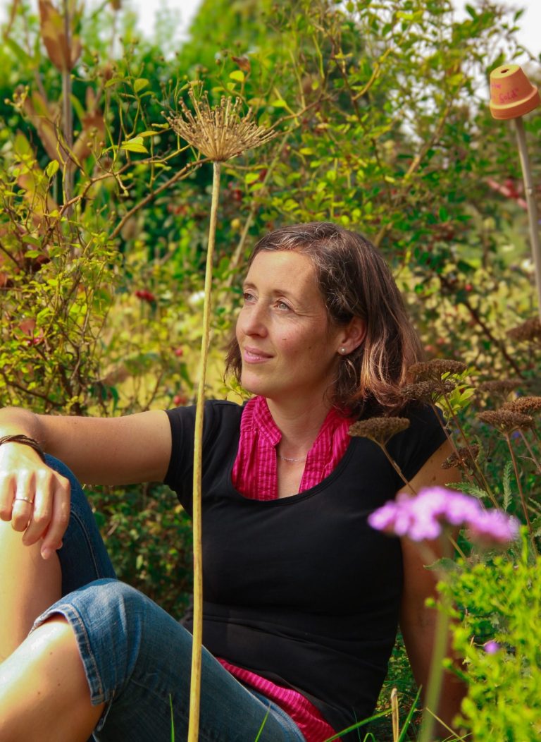 Businessporträt einer Gartengestalterin – aufgenommen in ihrem Garten, umgeben von Pflanzen und natürlicher Atmosphäre.