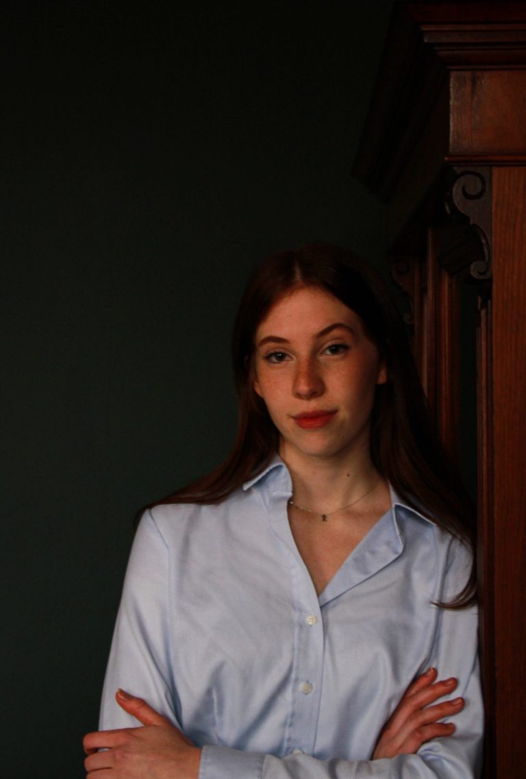 Stilvolles Bewerbungsfoto – elegante Frau, lässig an einem antiken Schrank lehnend, dunkler Hintergrund.