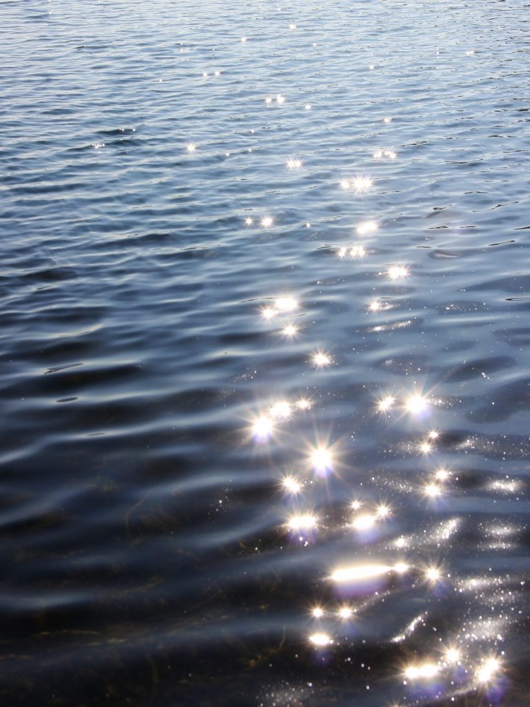 Künstlerische Naturfotografie – Sonnenlicht spiegelt sich auf Wasser und erzeugt funkelnde Lichtsterne.