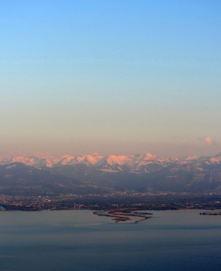 Luftaufnahme der Rheinmündung in den Bodensee – Blick aus einer Piper auf das Wasser und die Alpen im Hintergrund.